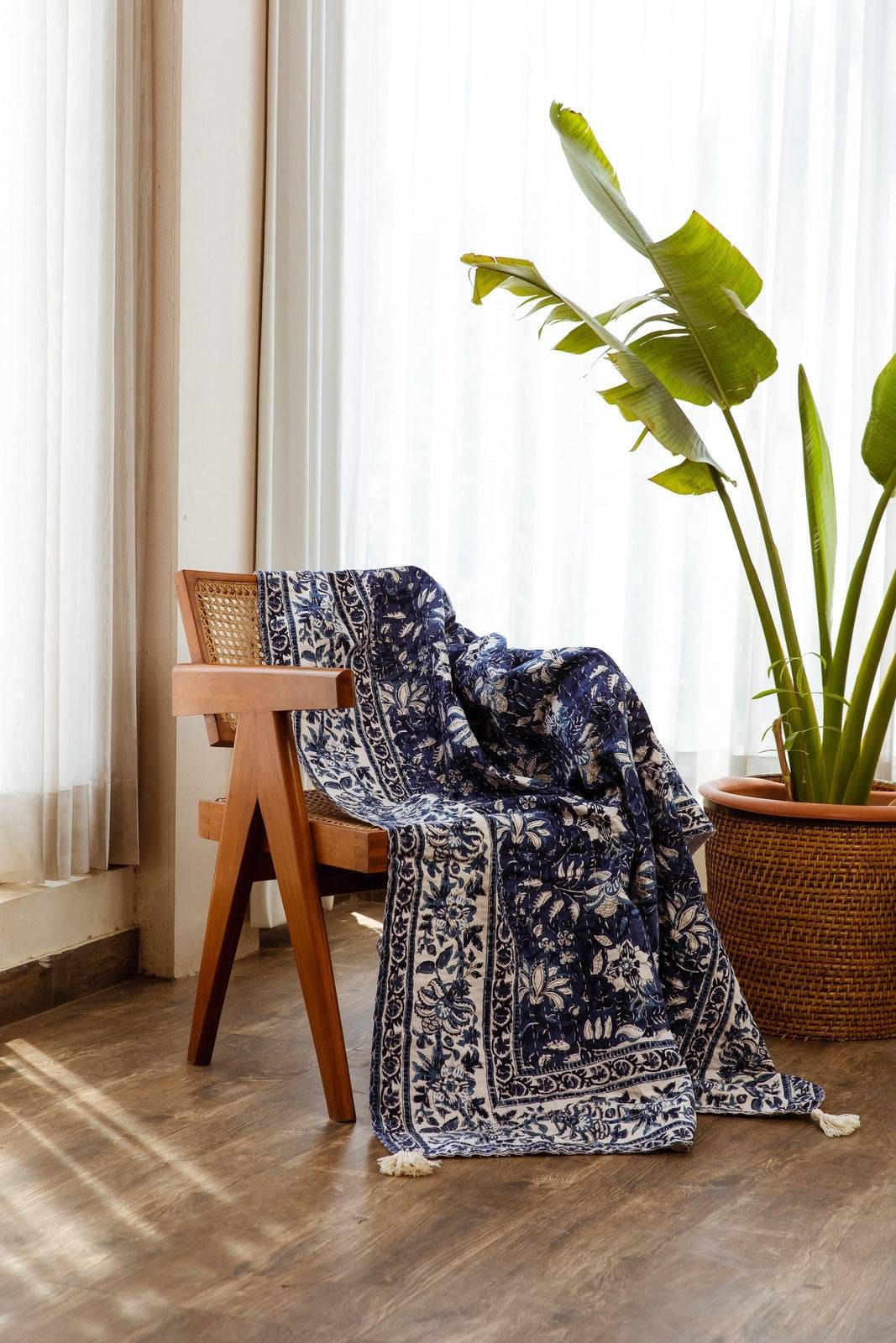 Blue patterned throw blanket draped over a chair in a room with curtains and a plant.