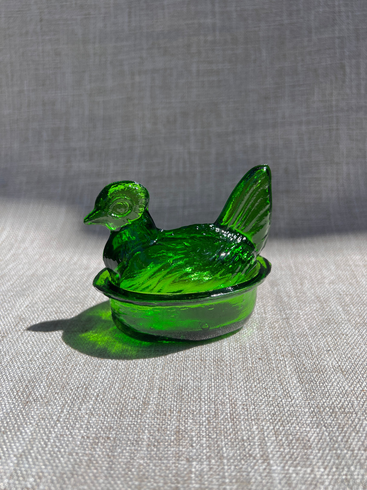 Green glass hen-shaped container on a gray fabric background