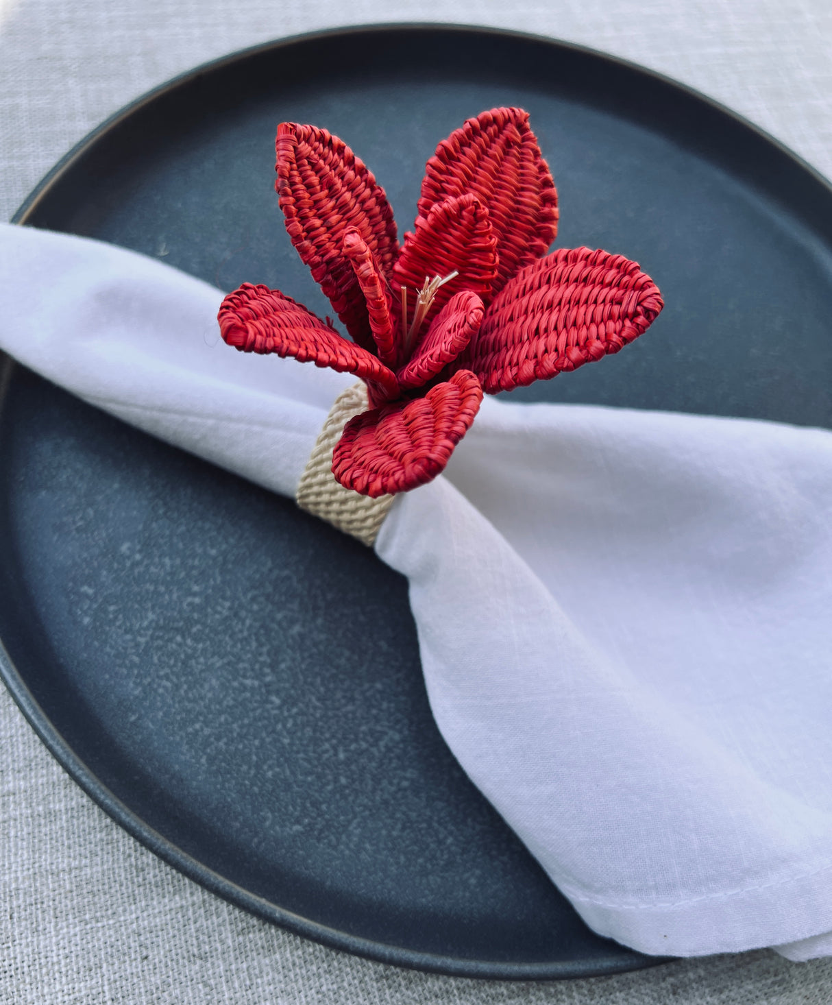 Red floral napkin ring on a white napkin over a black plate