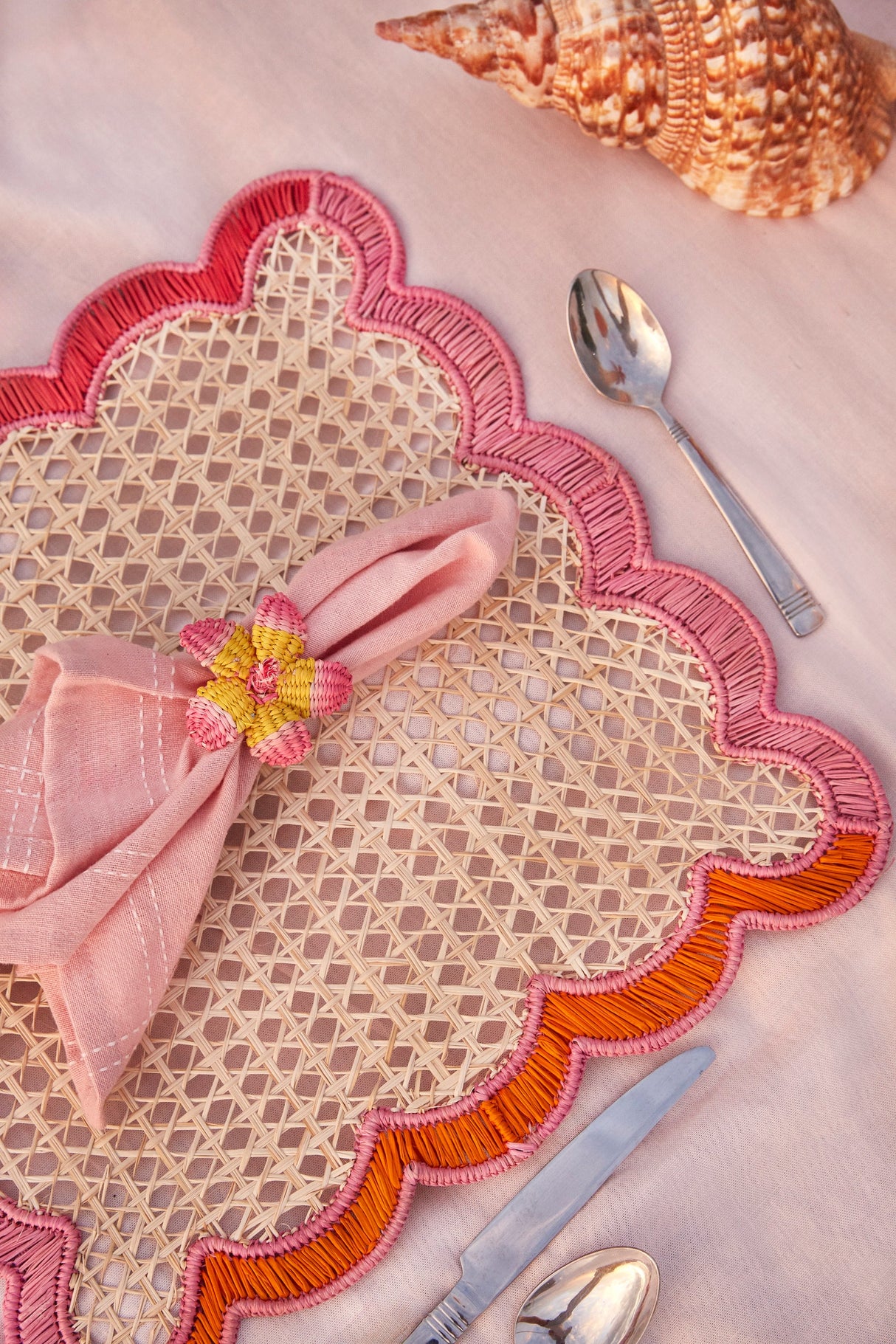 Decorative placemat with pink napkin and floral napkin ring on a pink surface.