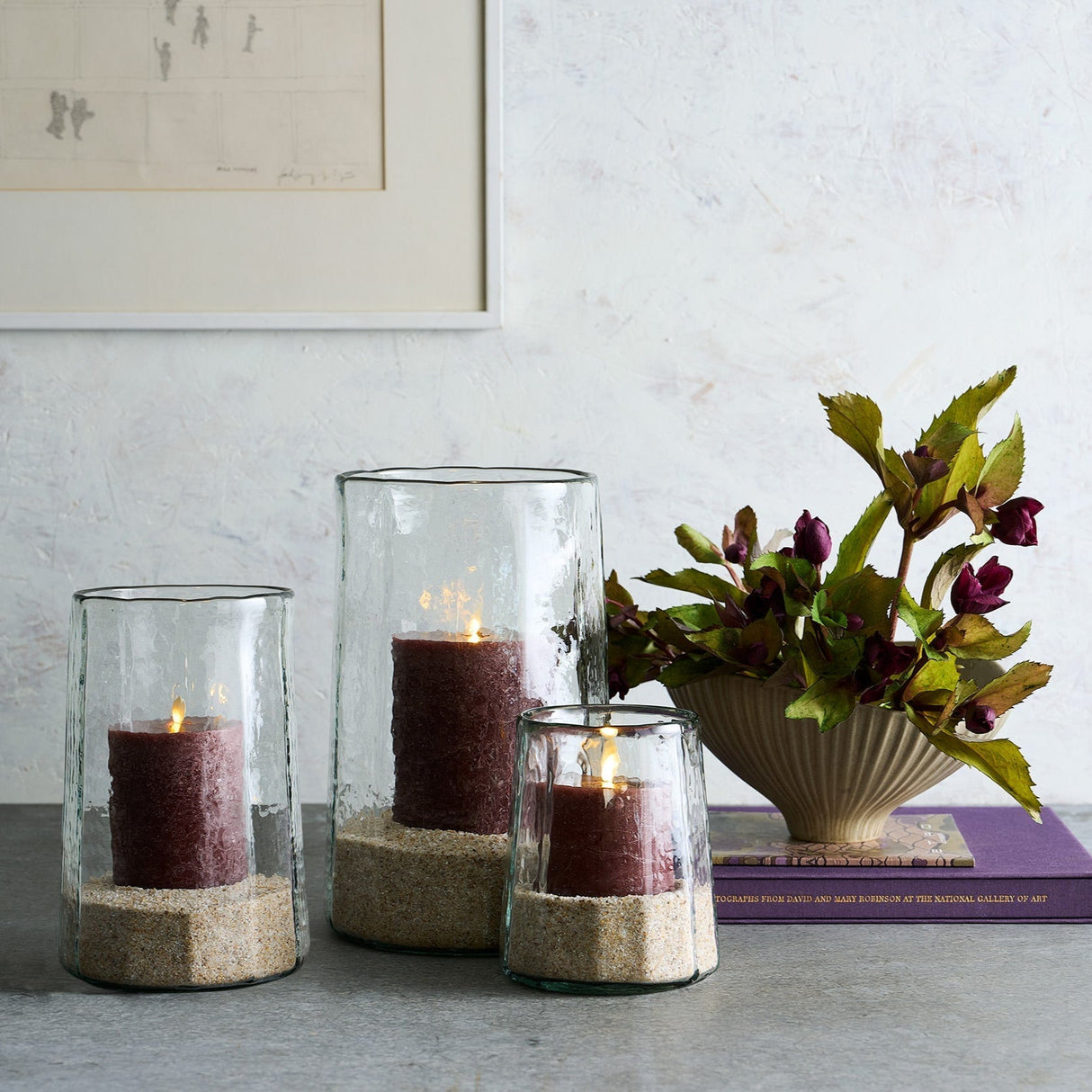 Decorative candles in glass holders on a table with a vase of flowers in the background.