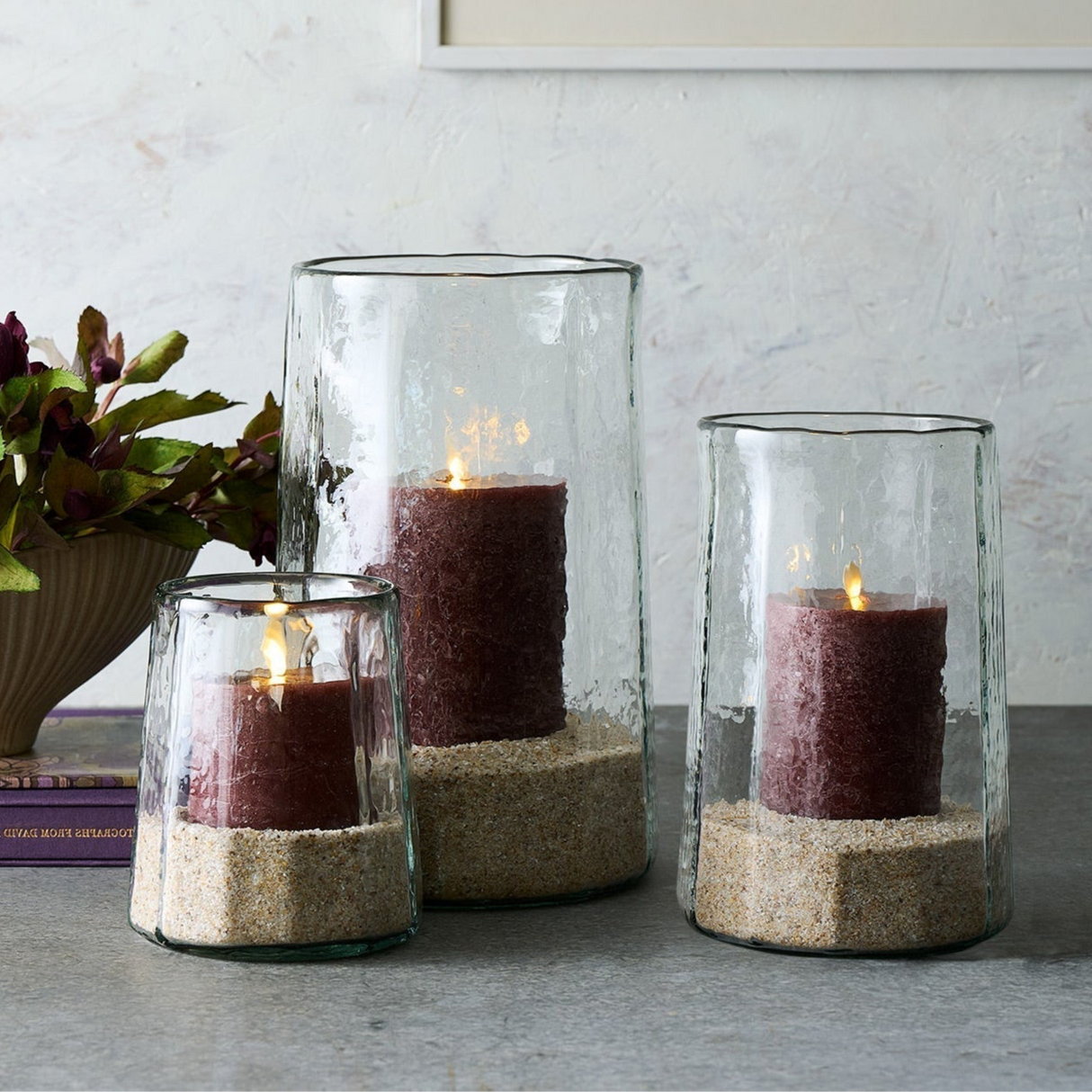 Three glass candle holders with sand and candles on a surface.