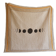 Decorative quilt with moon phase design on a wooden floor against an orange wall.