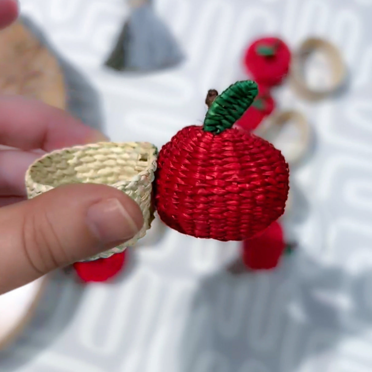 Red woven apple-shaped hair clip held by a hand with blurred background
