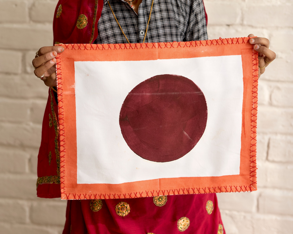 Woman holding a red and white flag with a large red circle on a white background against a light brick wall.