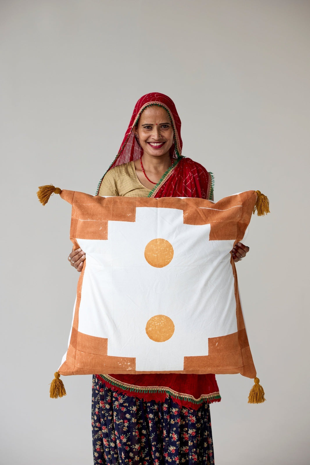 Woman holding a decorative pillow with a white center and brown border, featuring tassels.