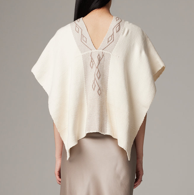 Woman wearing a cream-colored poncho with intricate patterns on a plain background