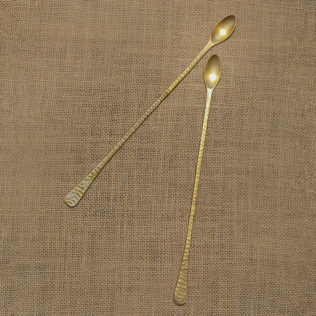 Two gold spoons on a textured brown fabric background