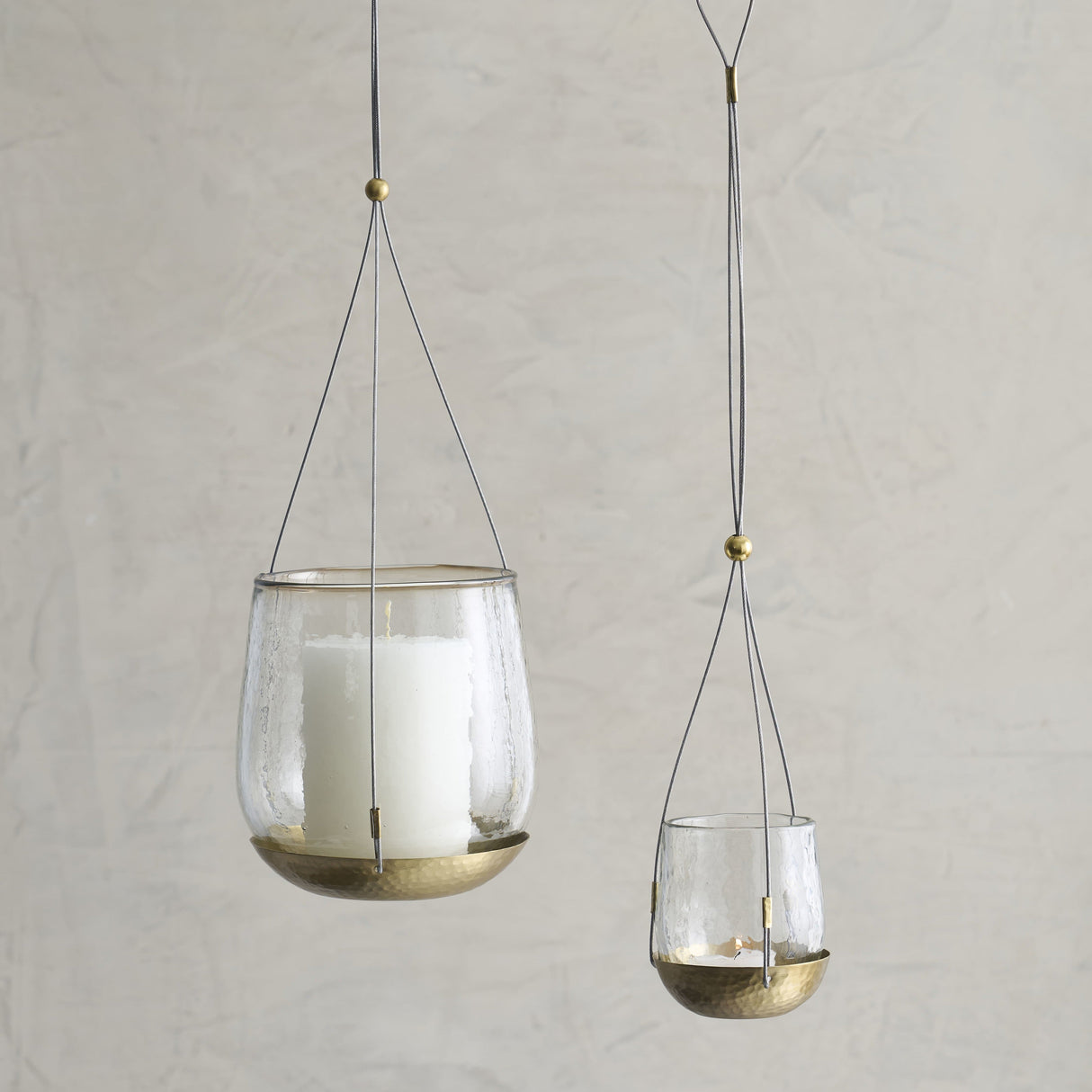 Two hanging glass candle holders with gold accents on a neutral background