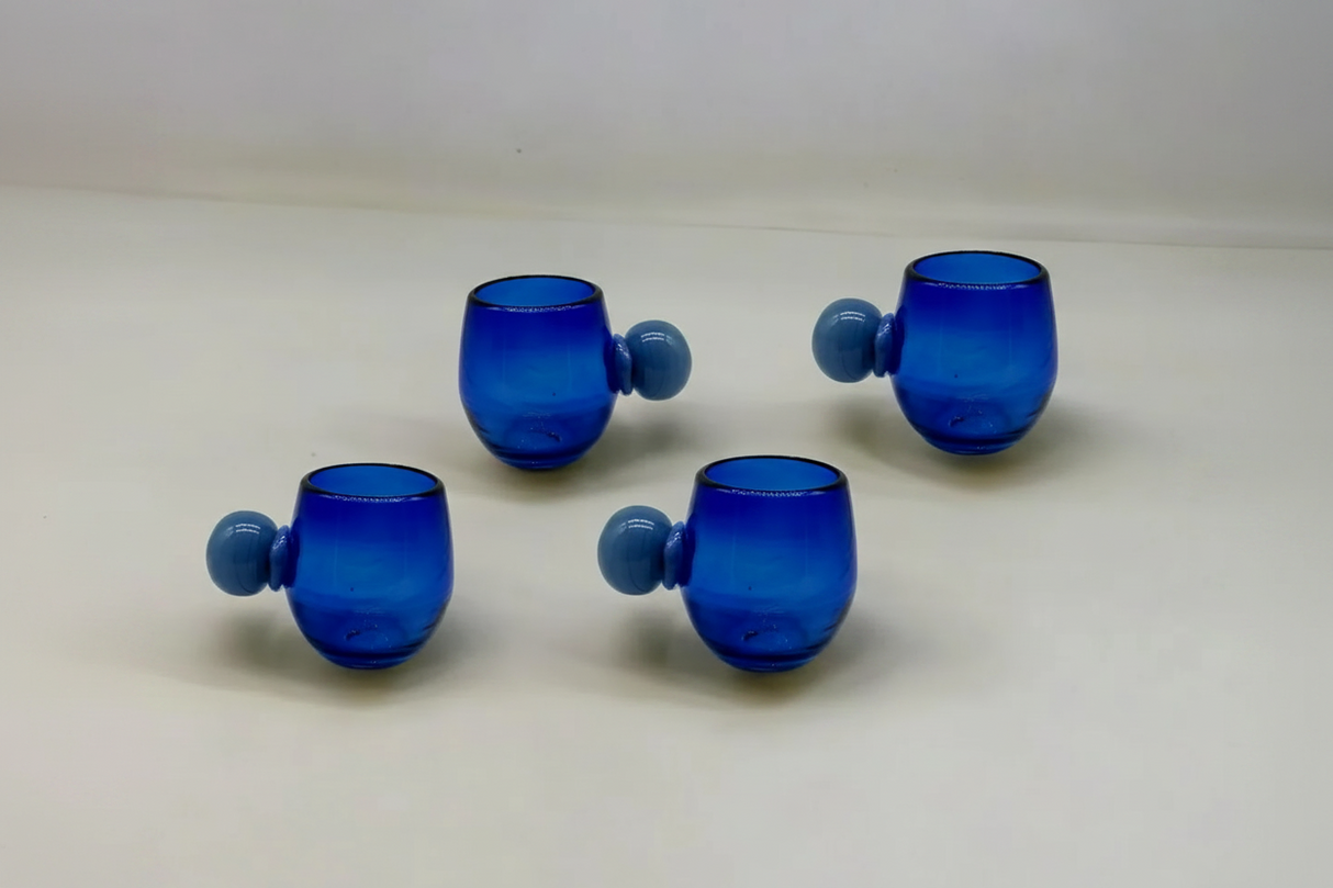 Four blue glass tumblers with spherical handles on a white background