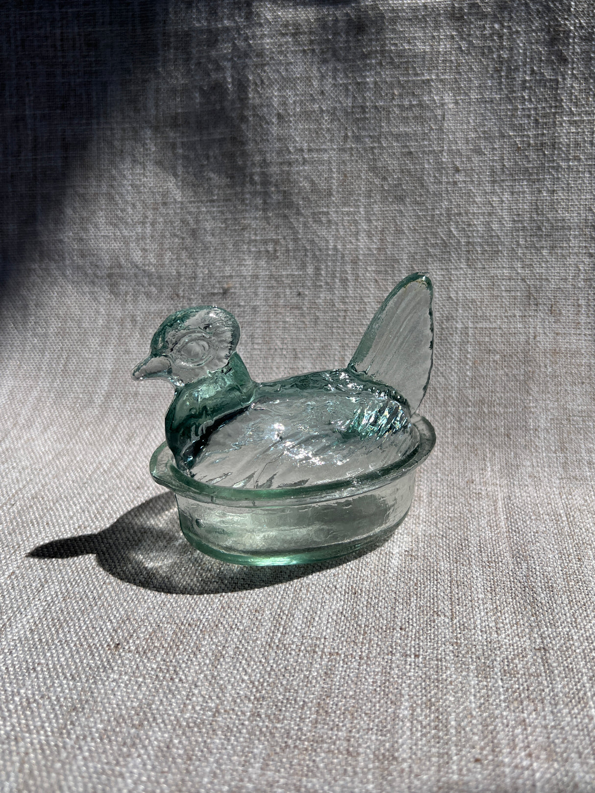 Glass object resembling a nesting hen on a textured fabric background