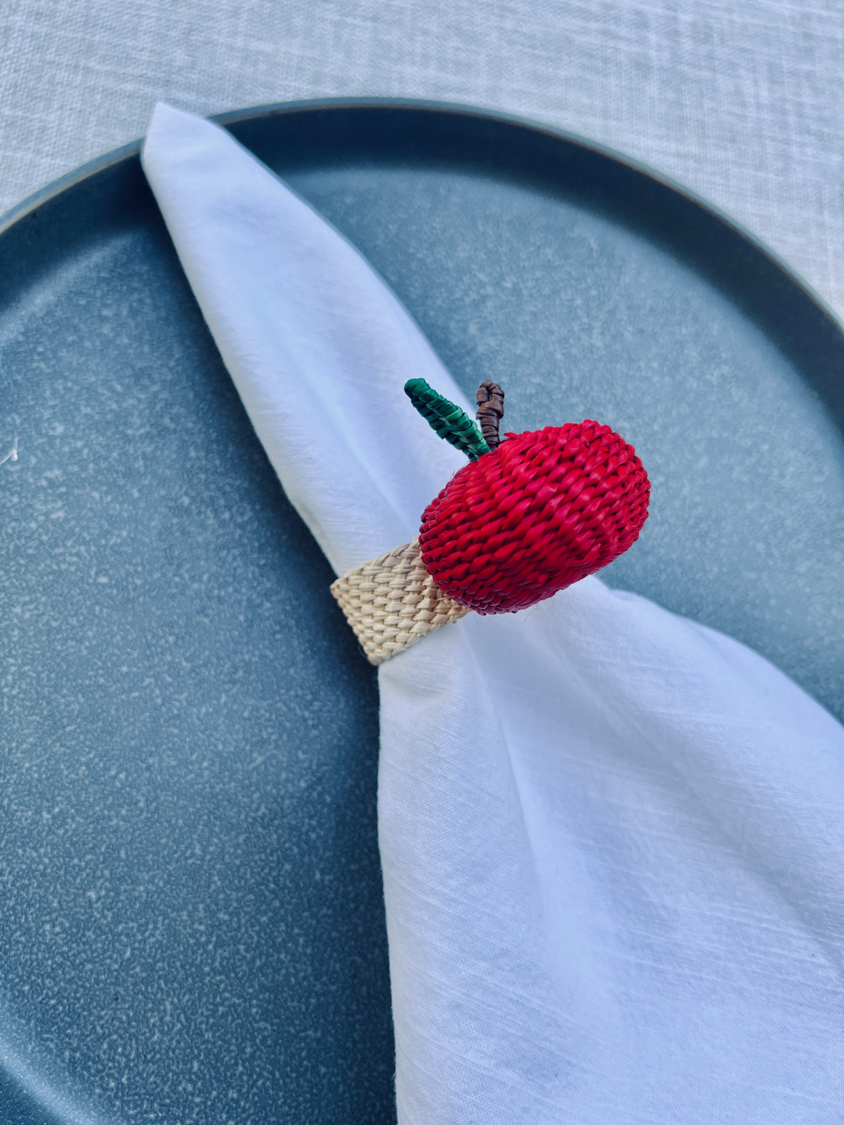 Crocheted apple napkin ring on a white napkin with a blue plate background