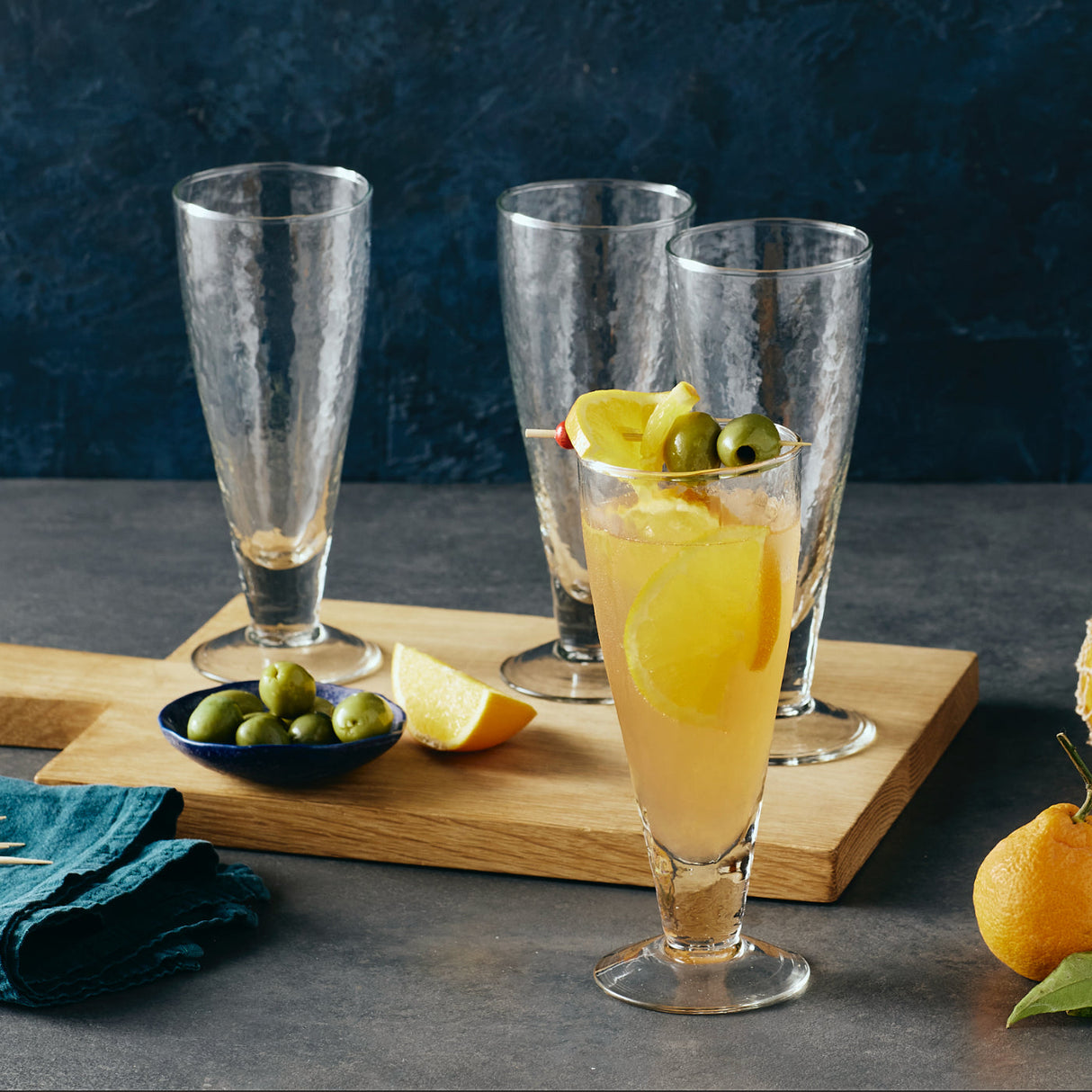Cocktail glasses with lemon slices and olives on a wooden board against a dark background