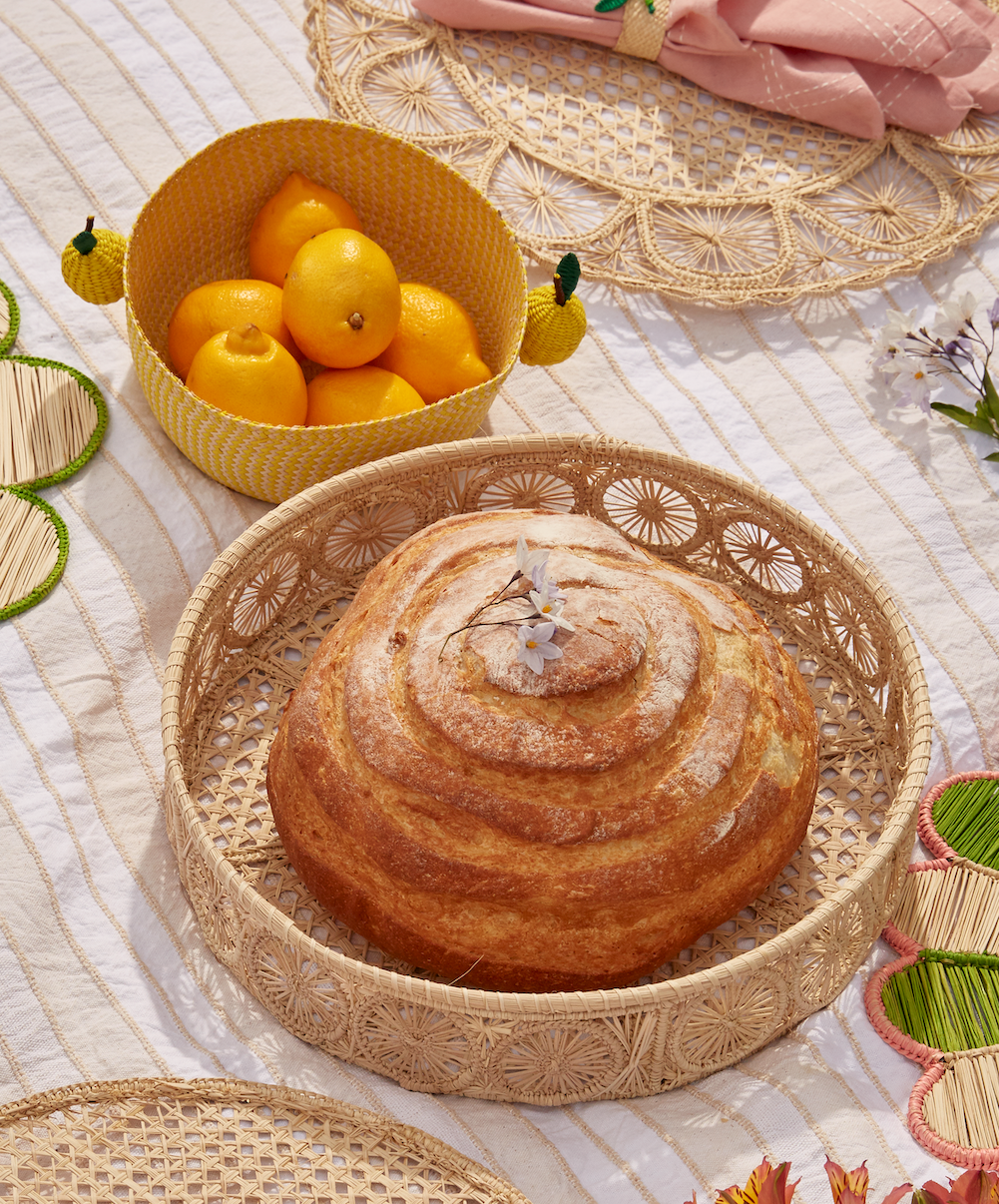 Loaf of bread on a woven plate with a basket of lemons on a textured surface