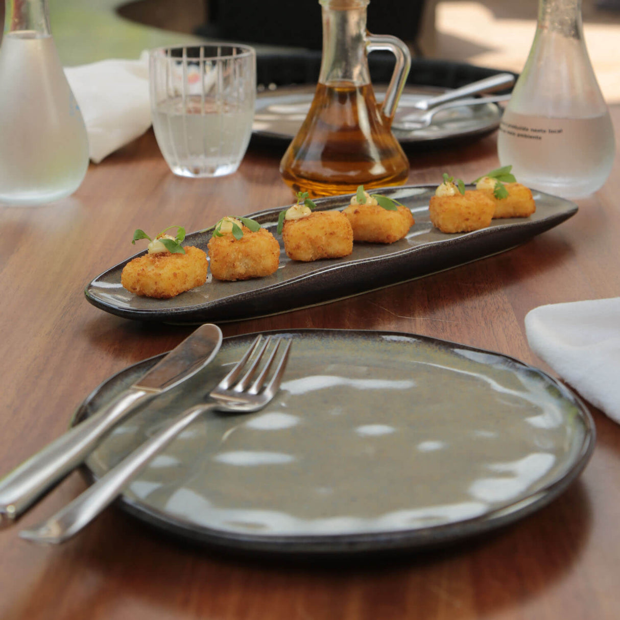 Dessert plate with small pastries on a wooden table with cutlery and water glasses.