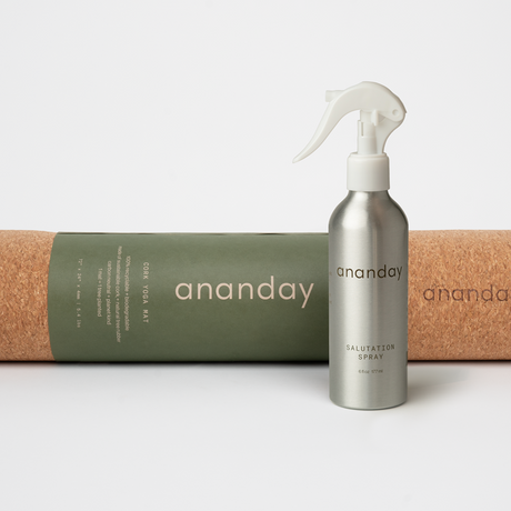 A rolled-up cork yoga mat next to a spray bottle labeled 'ananday' on a white background.