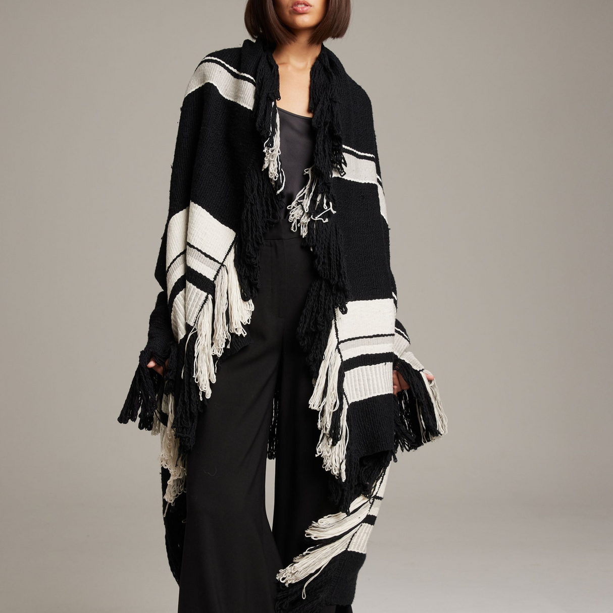 Person wearing a black and white striped scarf with fringe on a neutral background