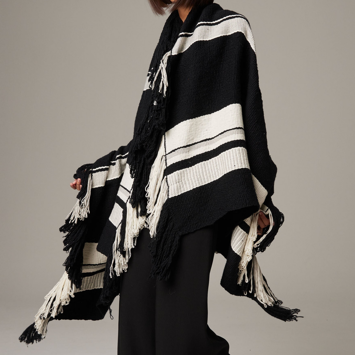 Person wearing a black and white striped poncho with fringes on a plain background