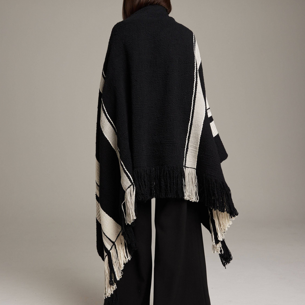 Black and white striped poncho with fringe details on a neutral background