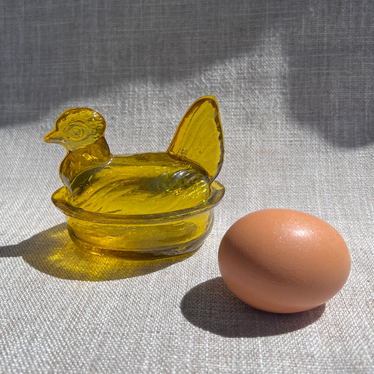 Yellow glass chick in a nest with a brown egg on a textured surface