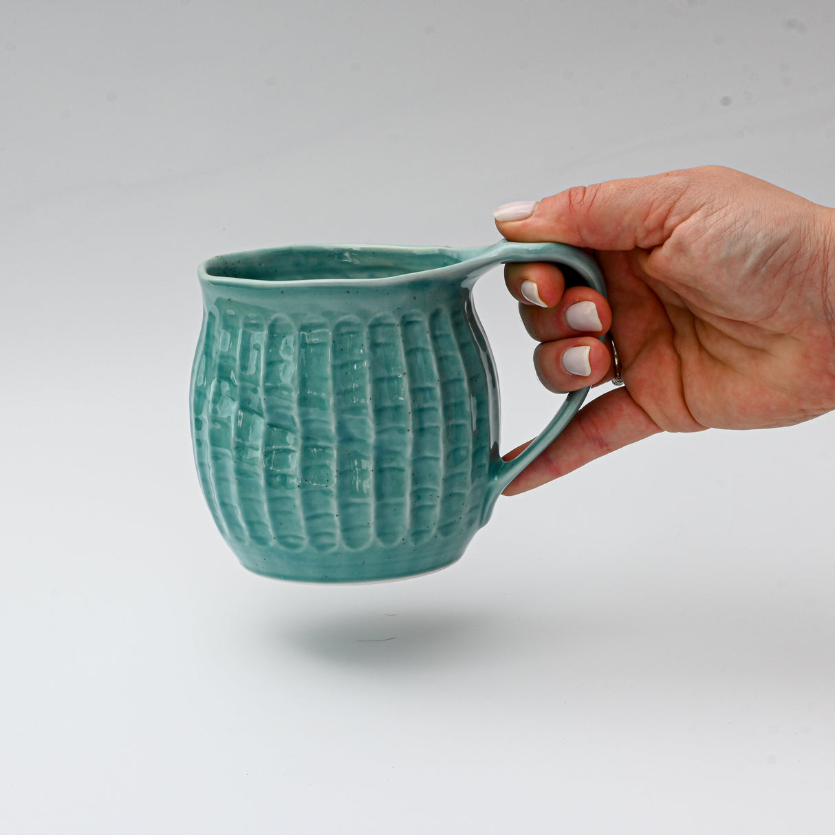 A hand displays a textured ceramic mug, "Handmade Big Blue Ceramic Tea or Coffee Mug from Japan - 18oz Capacity," set against a white background, highlighting exquisite Japanese craftsmanship.
