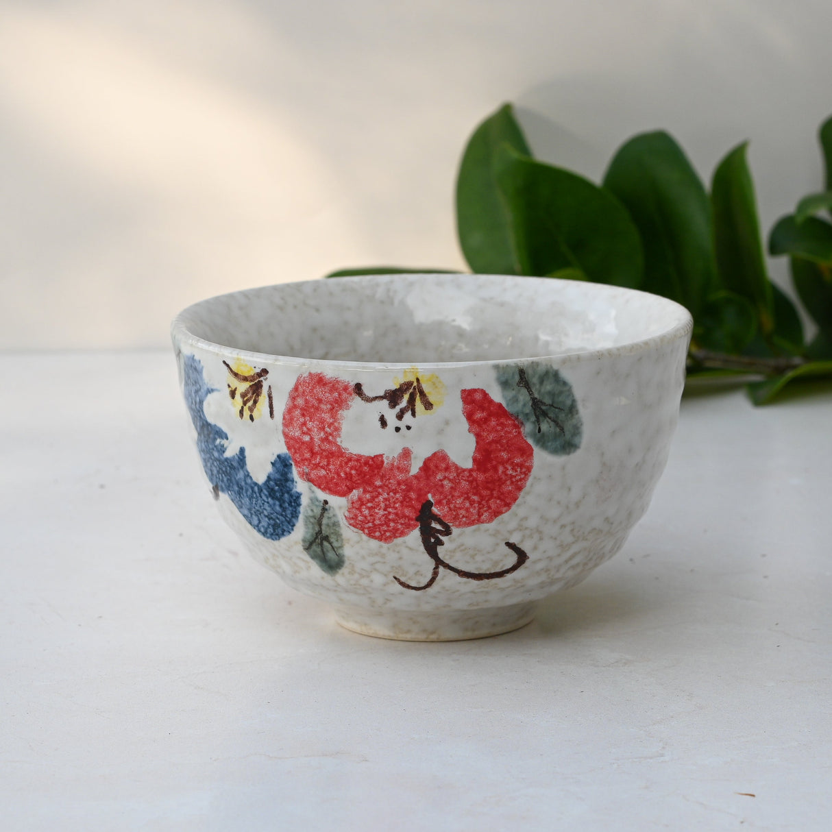 A Minoyaki ceramic matcha bowl featuring red and blue flowers with subtle leaves in the background.