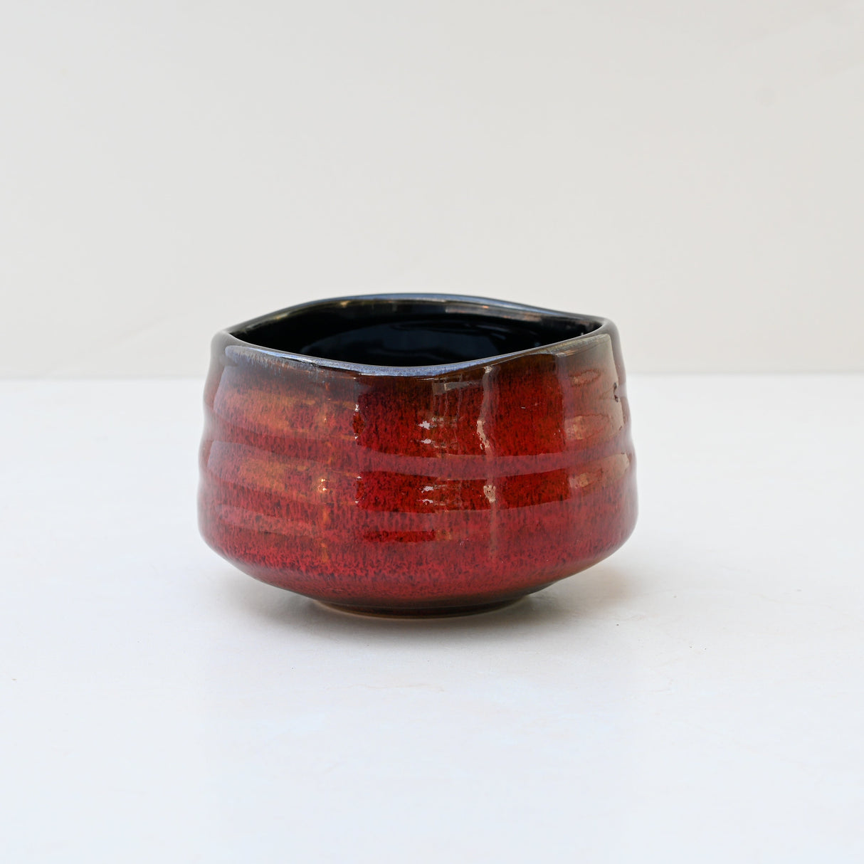 The Red Matcha Bowl resembles traditional Minoyaki Pottery with a textured red ceramic and black interior, elegantly resting on a white surface.