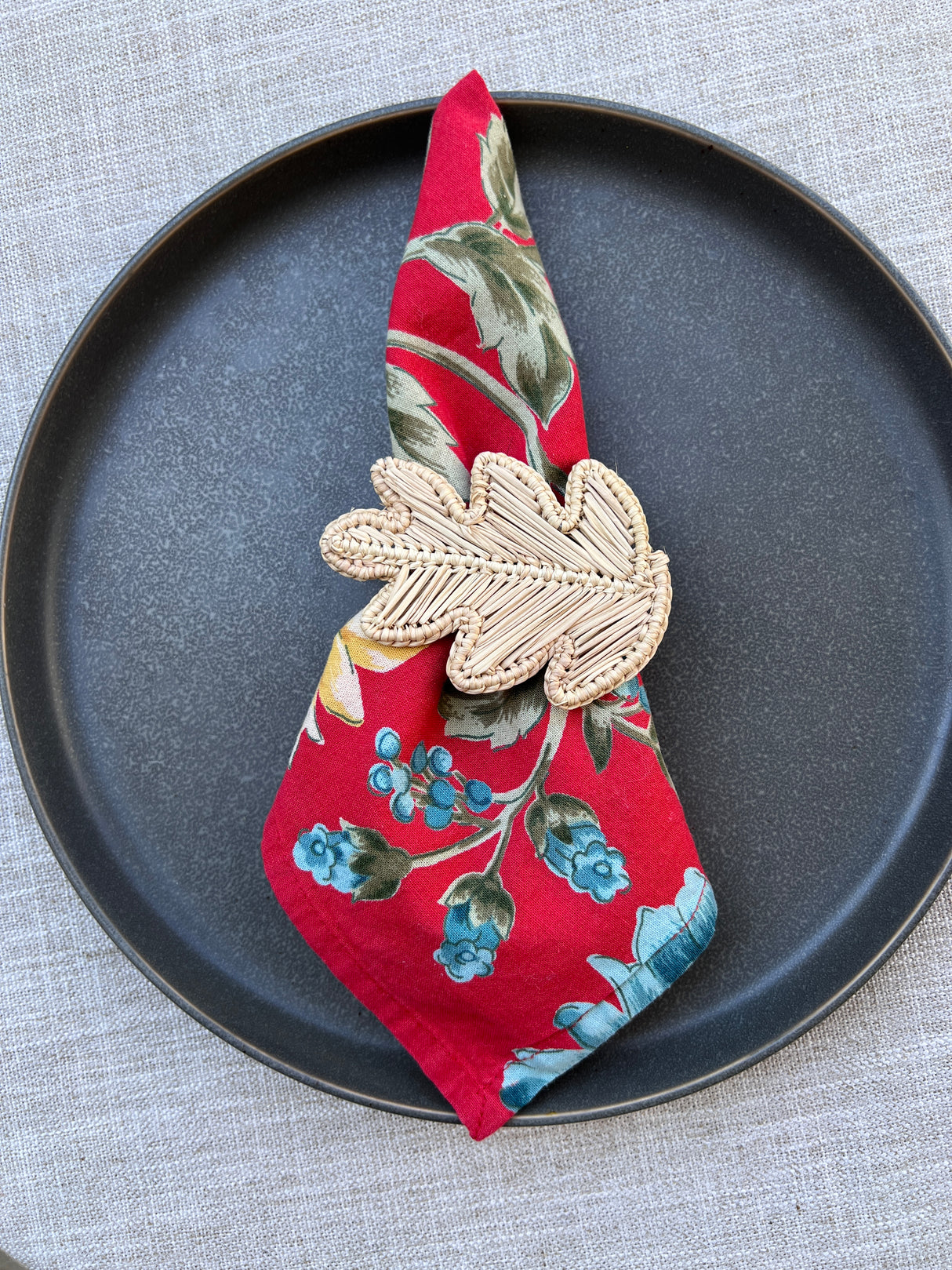 Decorative leaf napkin ring on a floral-patterned fabric on a black plate.