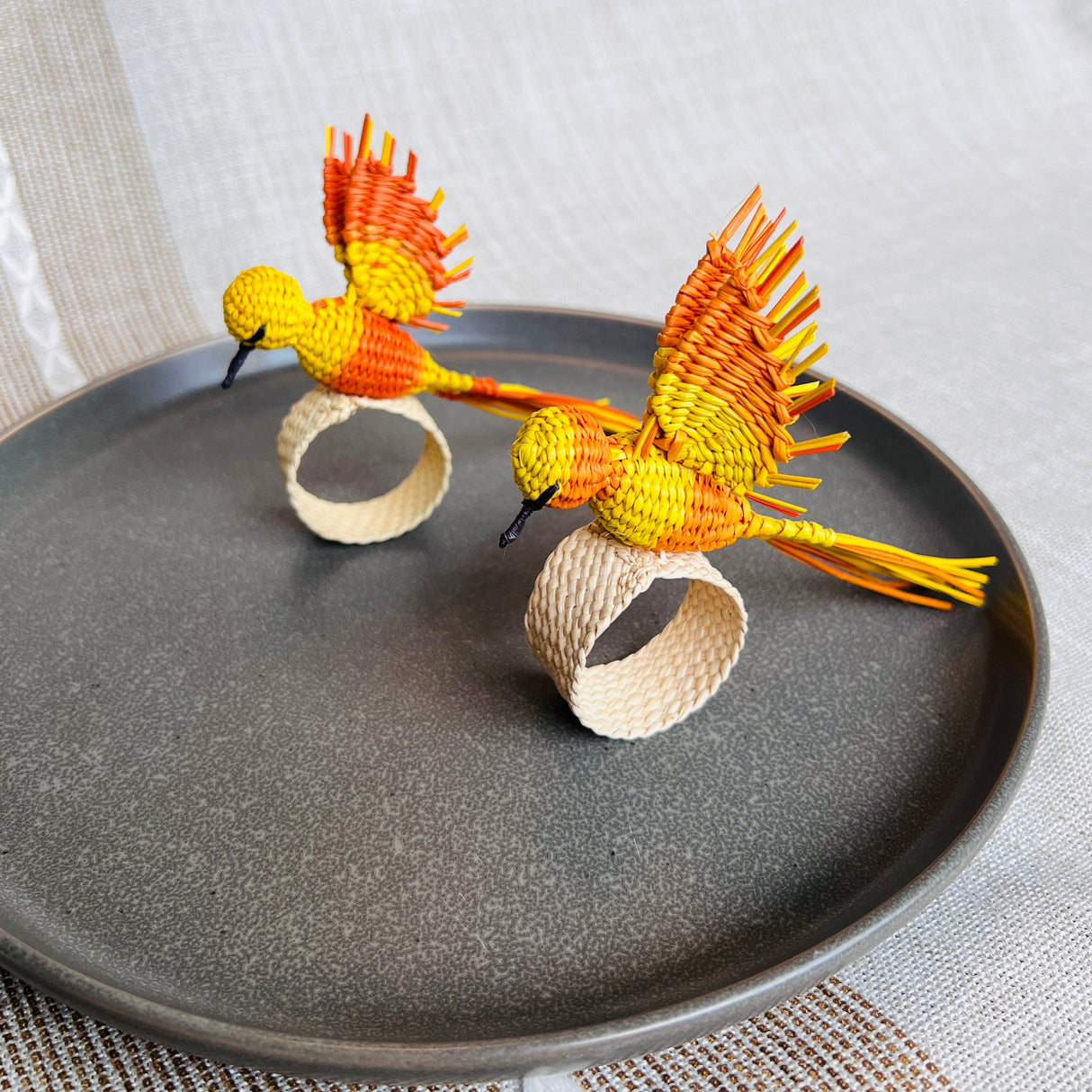 Two woven bird napkin rings on a dark plate with a light background