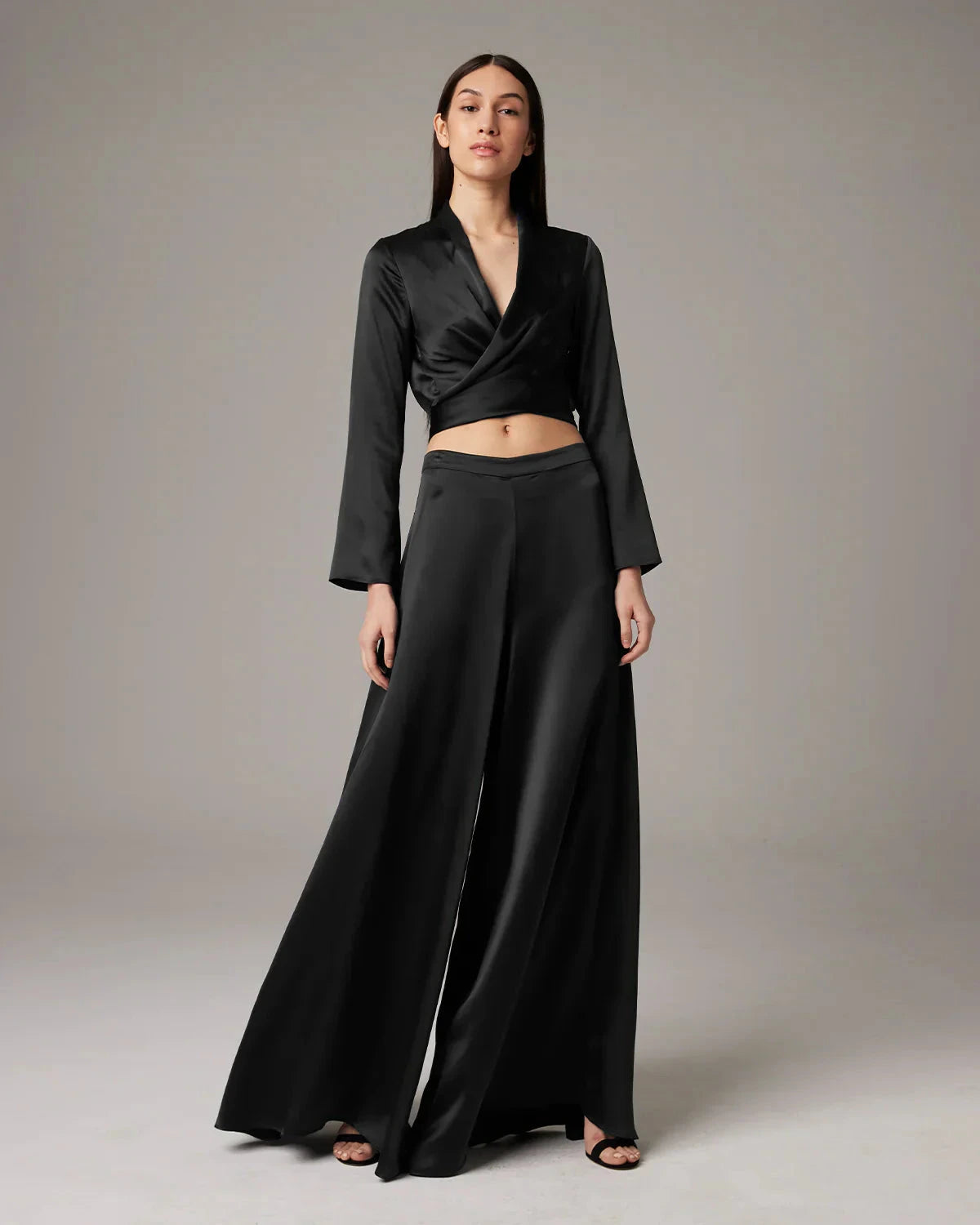 Woman wearing a black outfit with a long skirt and top on a plain background