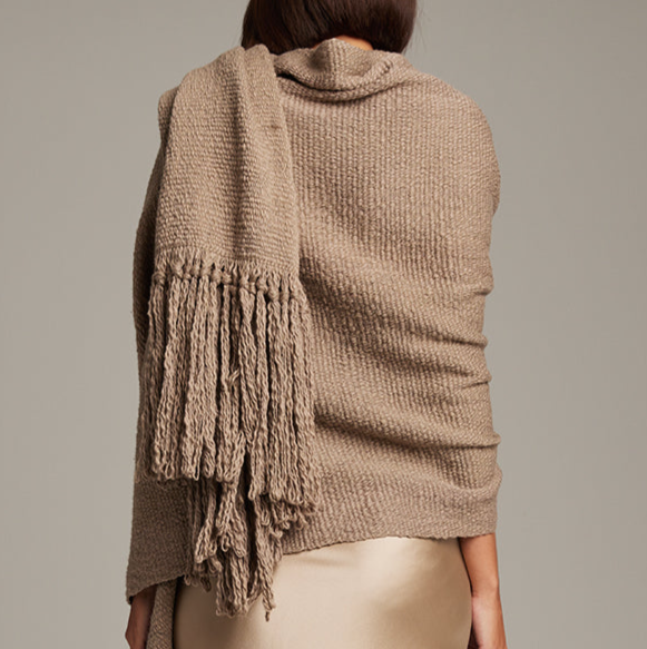 Person wearing a brown knitted sweater with a matching shawl on a plain background