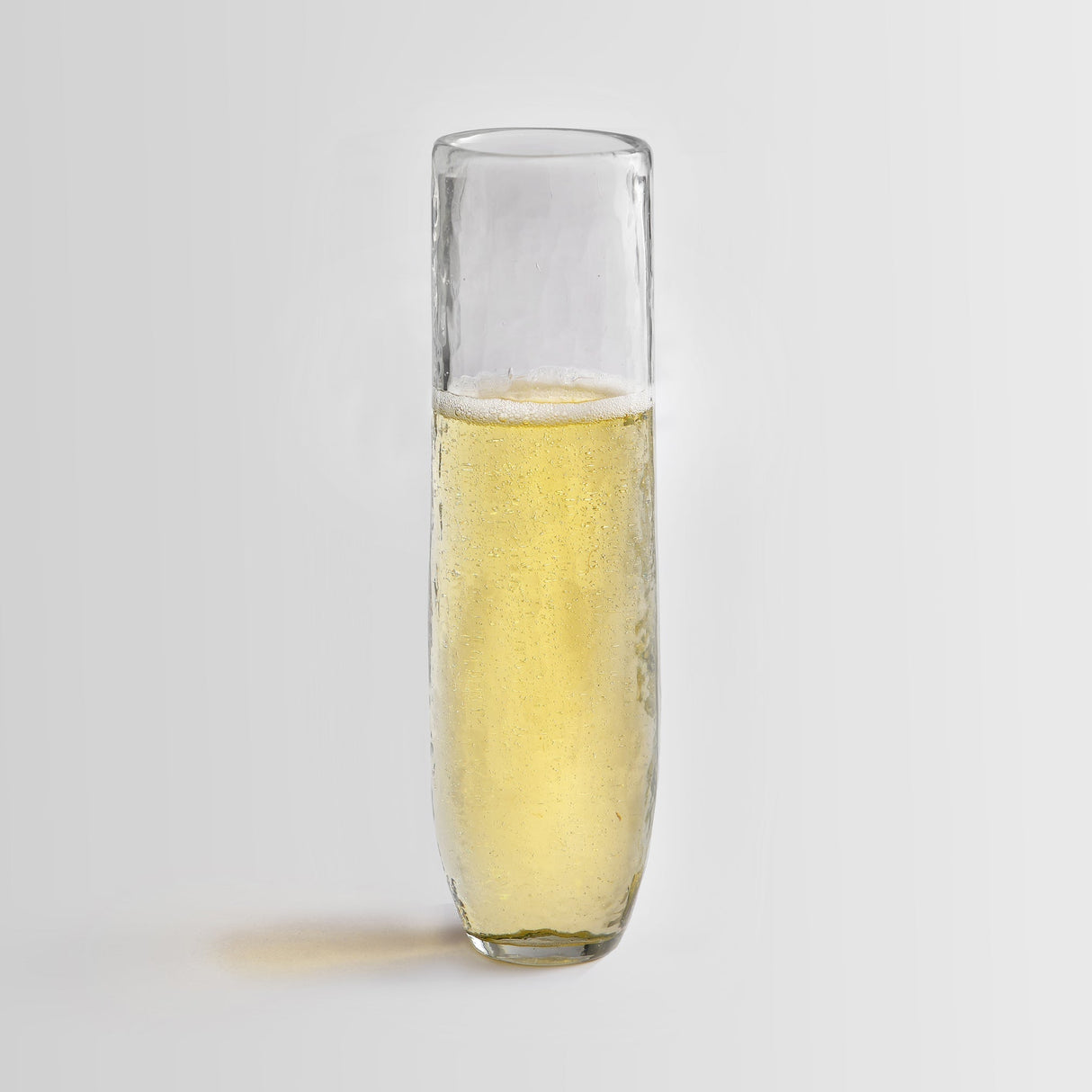 A single stemless flute filled with a bubbly beverage against a white background.