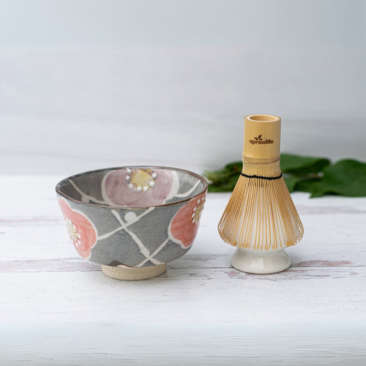 Gray ceramic matcha bowl with a floral design and bamboo whisk from the Japanese matcha set, displayed on a white surface.