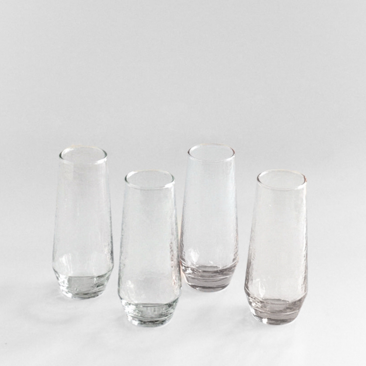 Set of four clear glass tumblers on a light gray background