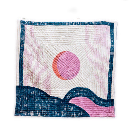 Quilt with pink sun and blue wave design on a white background