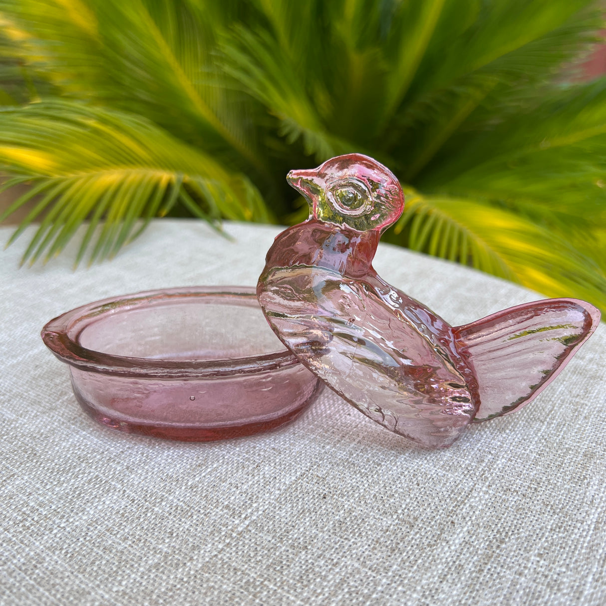 Pink glass bird-shaped container on a textured surface with green foliage in the background