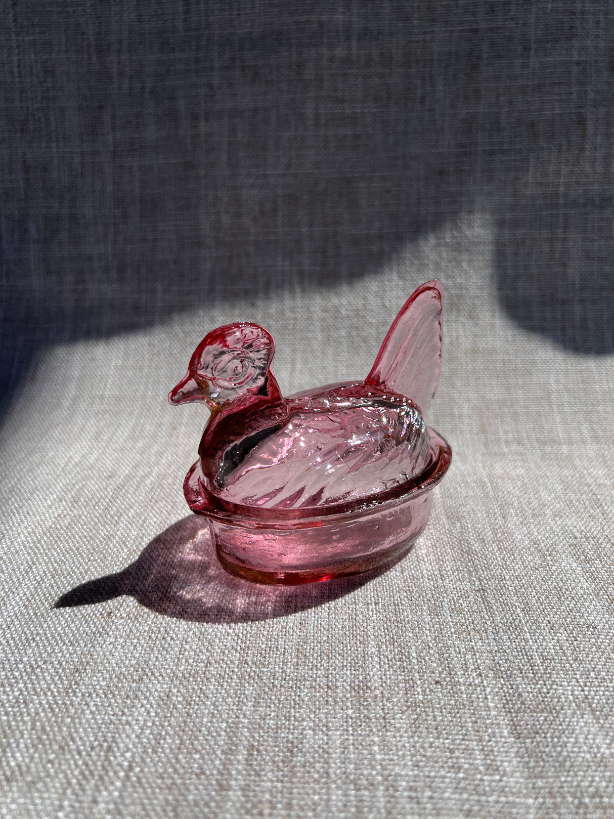 Pink glass nesting hen bowl & lid on a textured gray surface