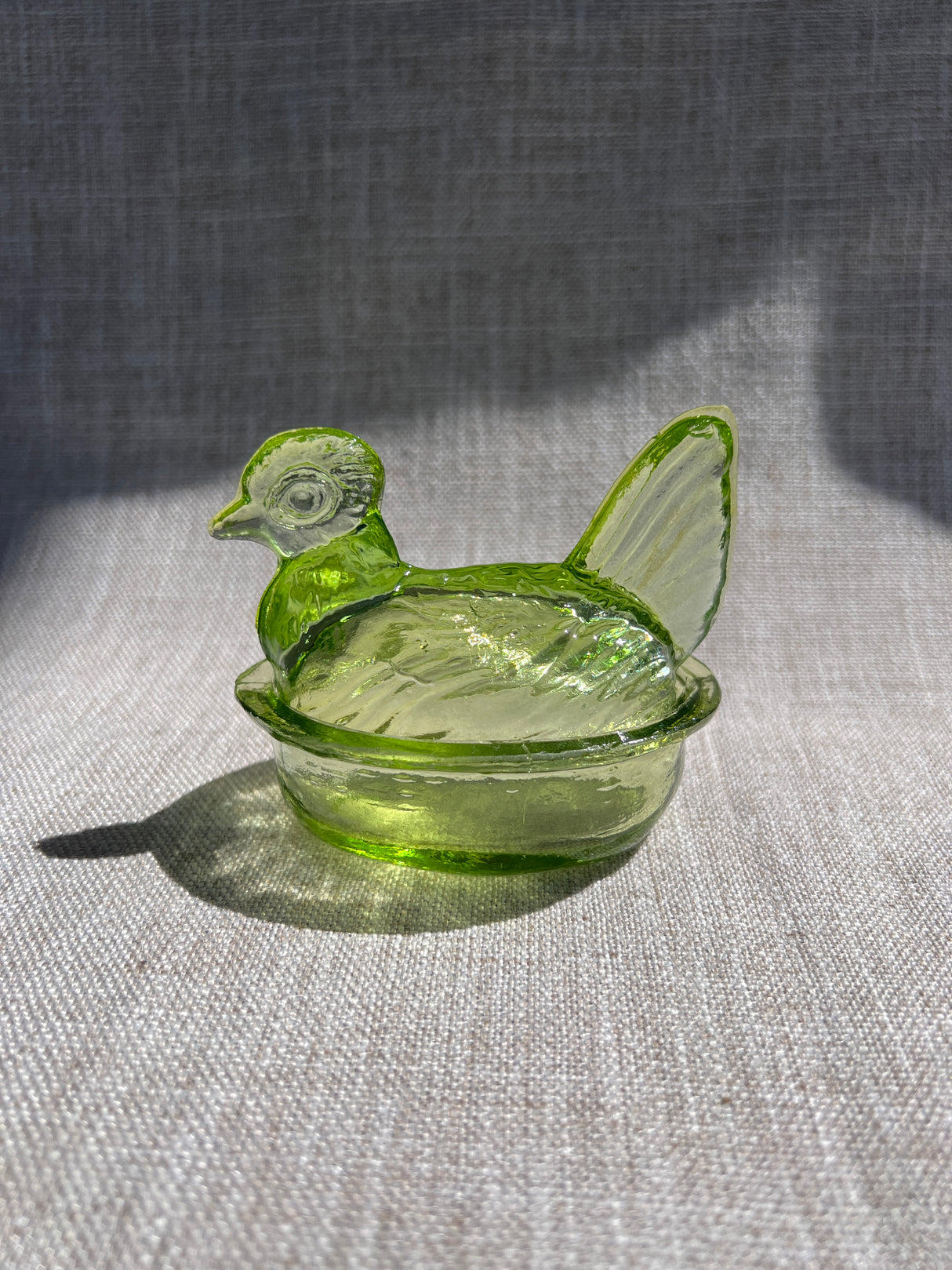 Green glass nesting hen bow & lid on a textured gray surface