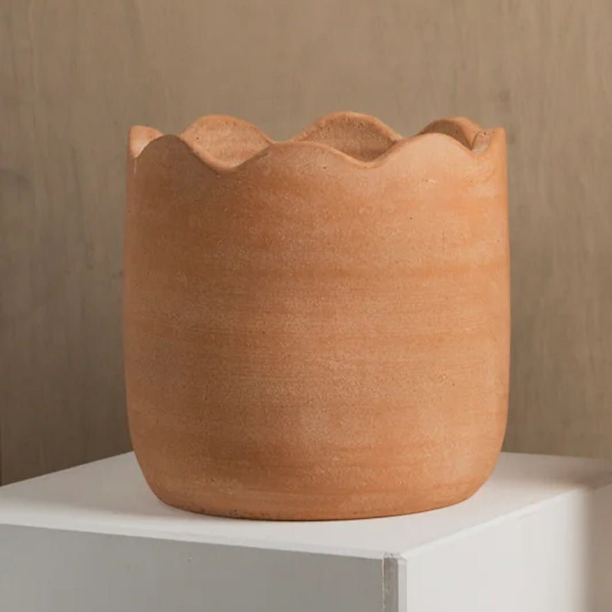Terracotta pot with wavy rim on a white surface against a beige background
