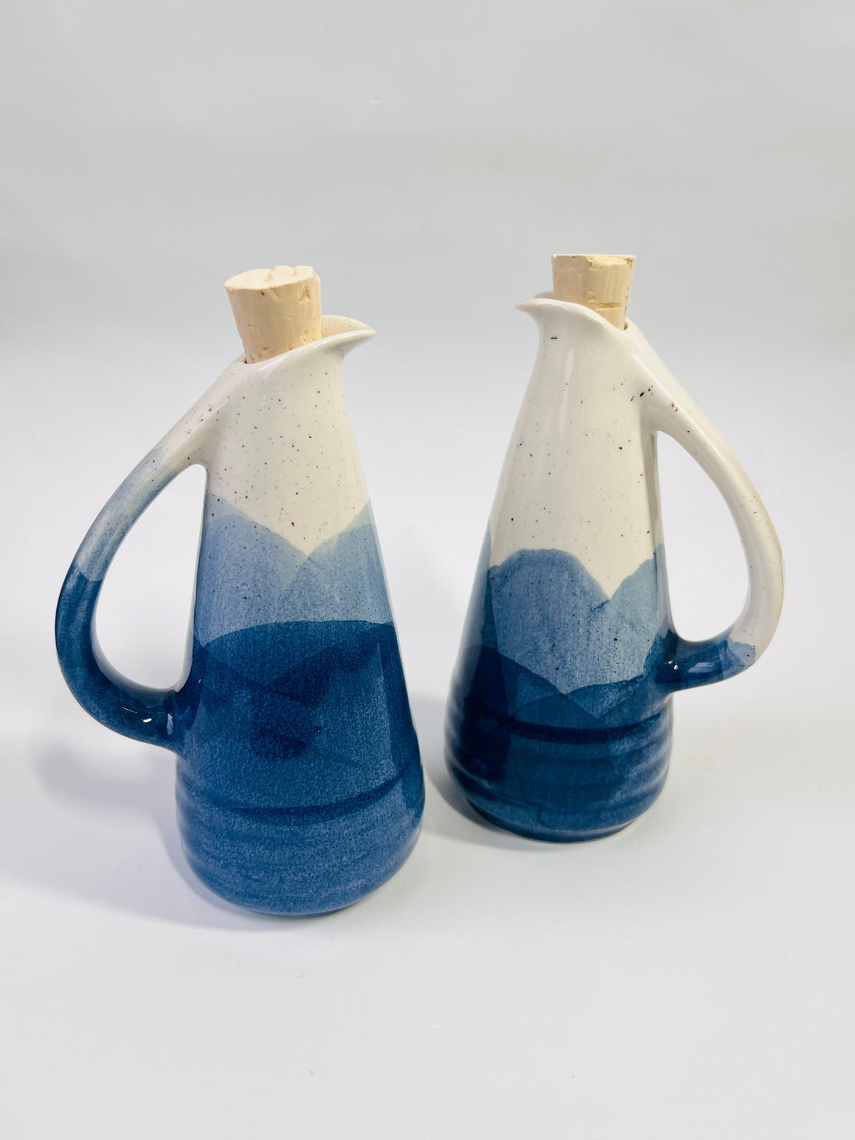Two ceramic pitchers with blue and white gradient design on a light gray background