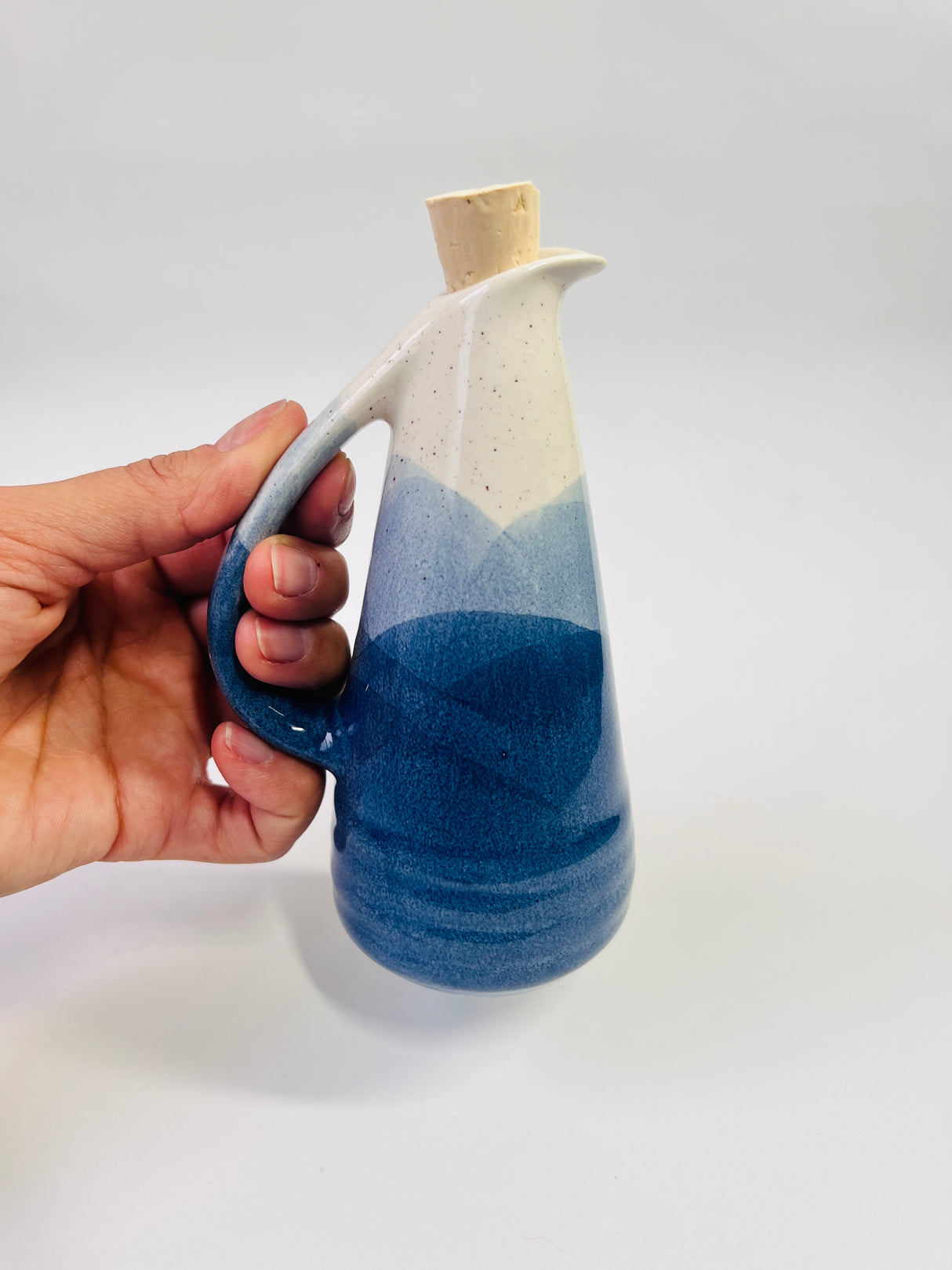 Hand holding a ceramic bottle with blue gradient design on a white background