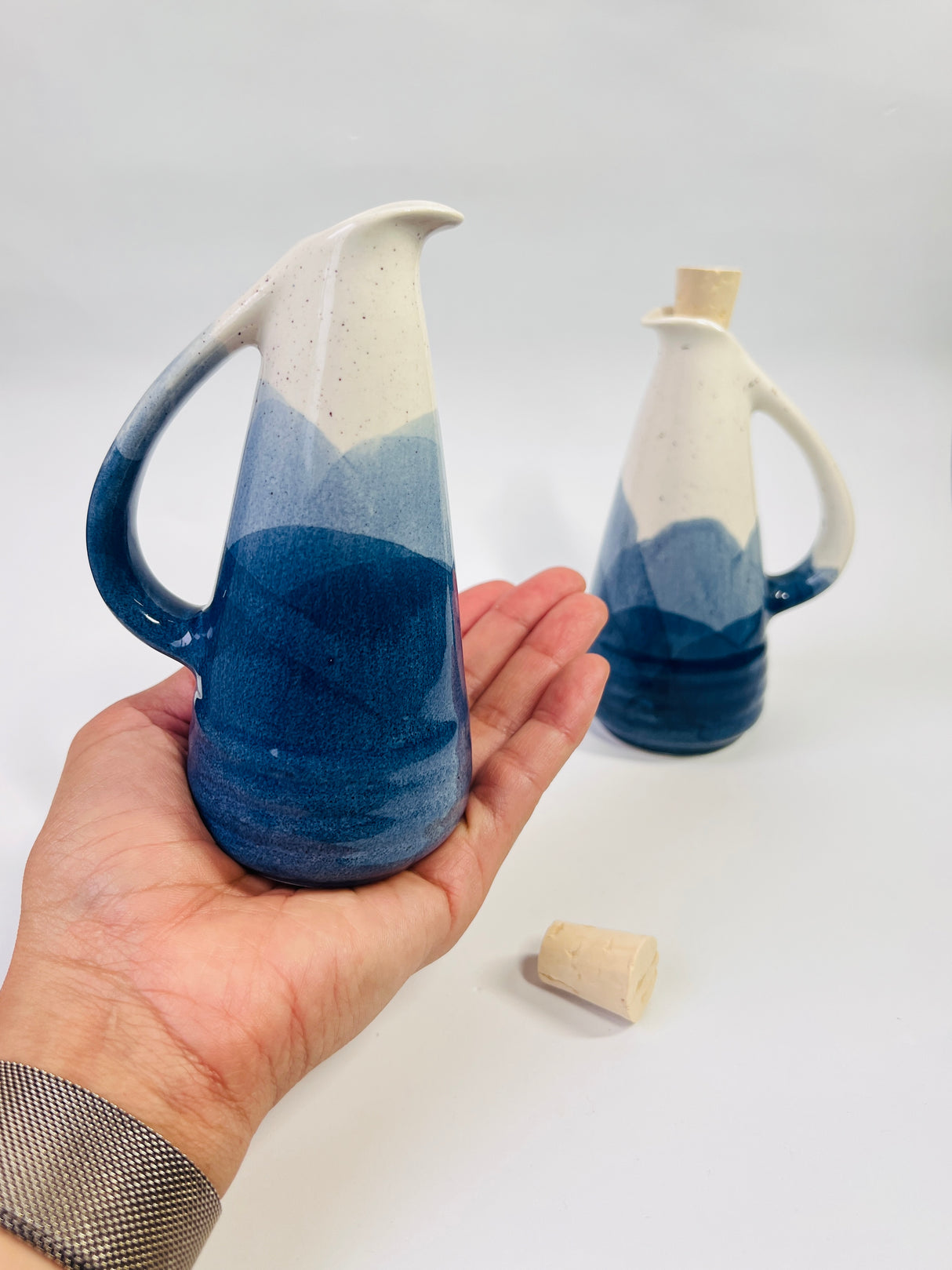 Ceramic pitcher with blue and white gradient held in a hand, with another pitcher in the background.