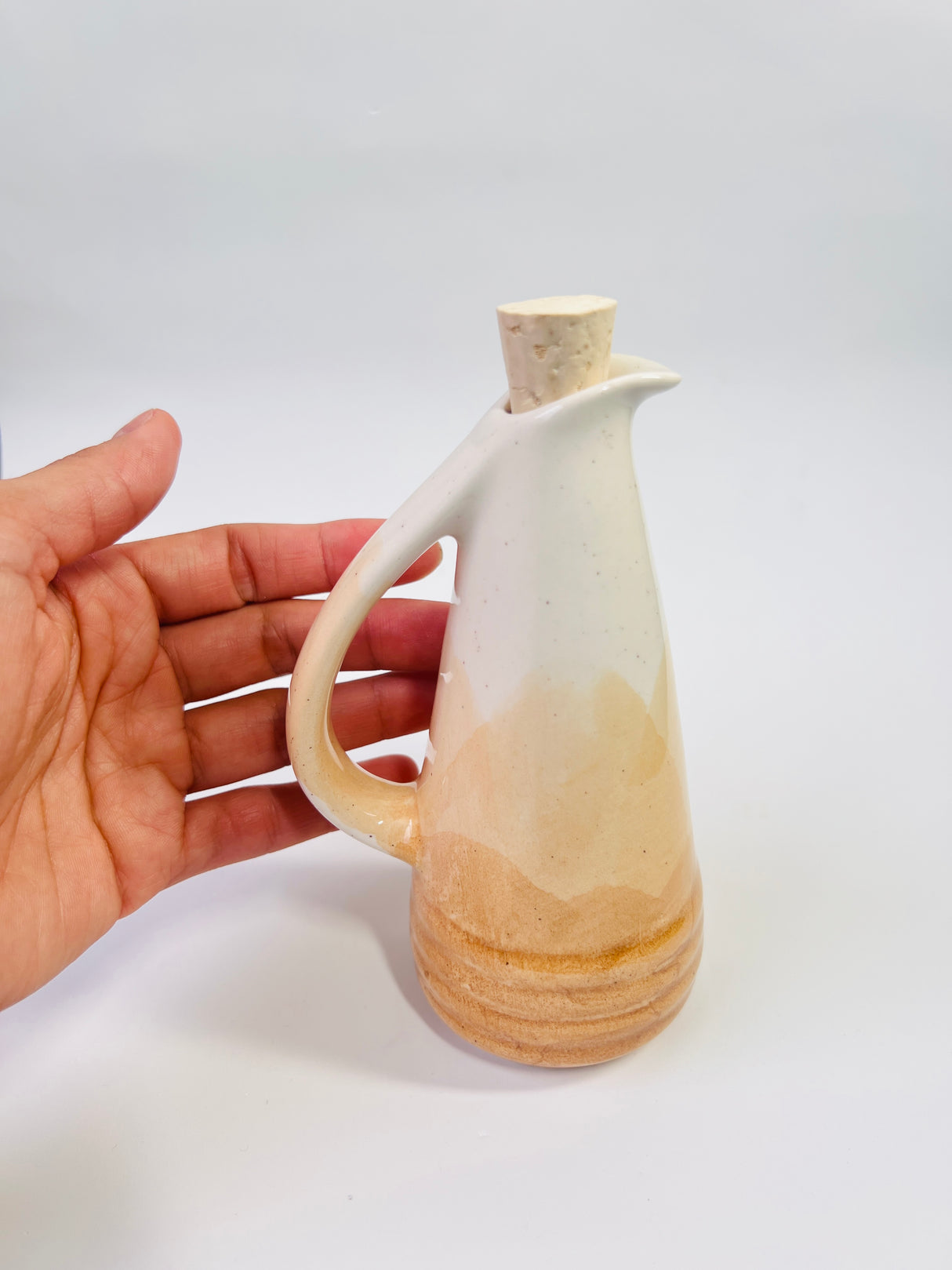 Hand holding a ceramic oil bottle with a gradient design on a white background