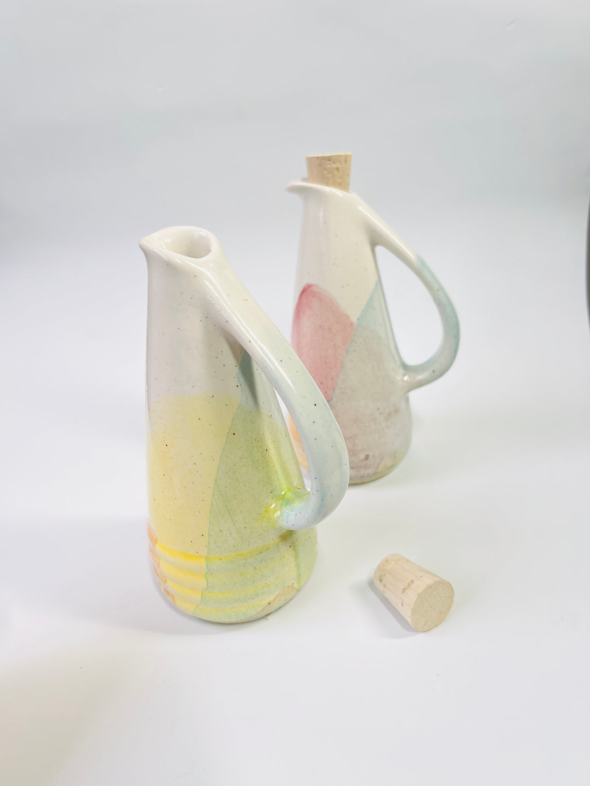 Two ceramic pitchers with cork stoppers on a white background
