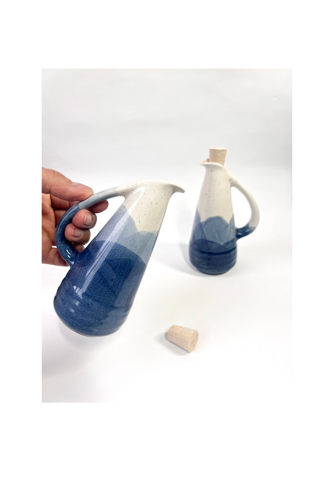 Ceramic pitcher with blue and white gradient held by a hand on a white background