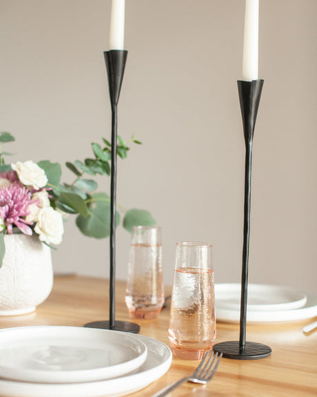 Black candle holders with white candles on a table setting with glasses and flowers.