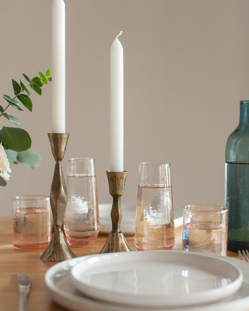 Dining table setting with candles, glasses, and a bottle on a neutral background