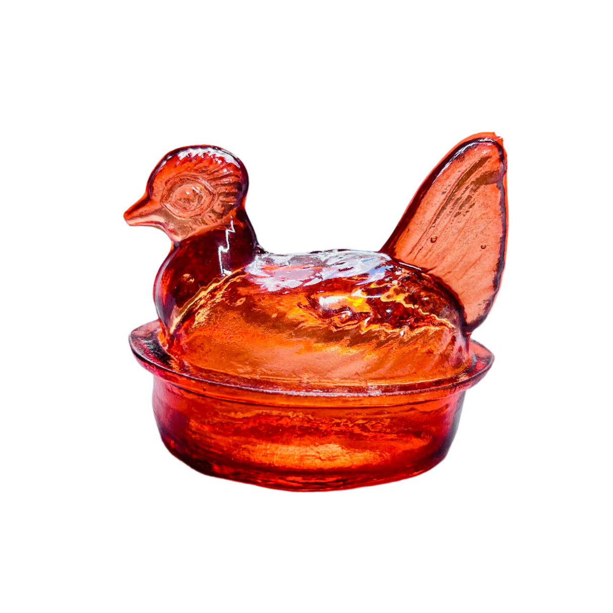 A tangerine orange hand blown glass nesting hen with a lid, on a white background.