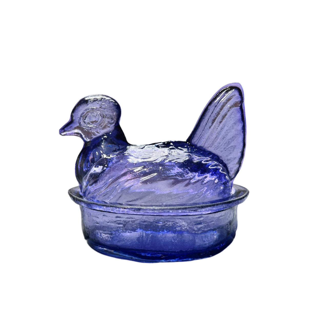 A hand blown glass bowl in the shape of a nesting hen with a lid, in a translucent lavender color.