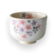 The Kohiki Pink Sakura Ceramic Matcha Bowl is a white ceramic bowl adorned with floral patterns in pink, purple, and gray on a black background, ideal for a traditional matcha tea ceremony.